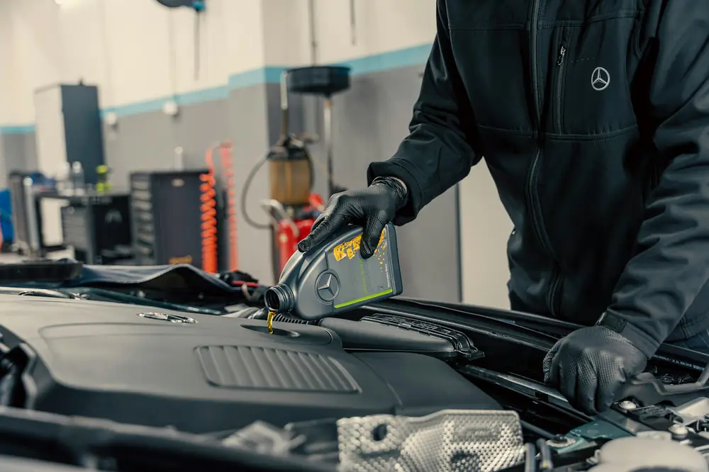 Mechanic in gloves pouring fresh oil into an engine